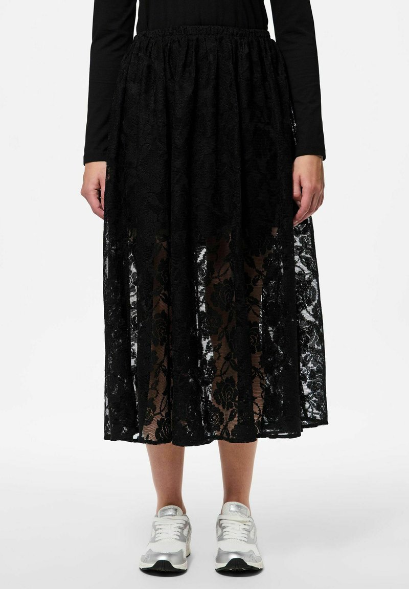 Jupe maxi en dentelle noire avec un motif floral, taille élastique, design superposé et texture transparente, associée à des baskets argentées.