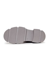 Suela exterior de goma gris con un diseño segmentado, que presenta una sección central lisa y franjas texturizadas para mejorar el agarre. Logotipo circular grabado en relieve.