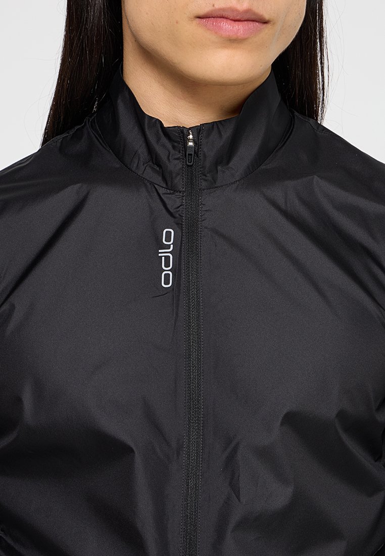 Czarna, lekka kurtka z wysokim kołnierzem, pełnym zamkiem błyskawicznym i wyraźnym białym logo po lewej stronie. Gładki, matowy materiał.