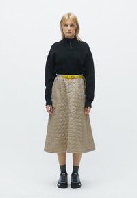 Melnā jaka ar rāvējslēdzēju, beigu pārklāta midi svārki ar dzelteno jostu, melnas kurpes. Gluda tekstūra, taisnstūra pārklāšanas raksts un izteikta forma.