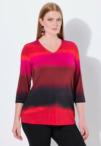 Rotes und pinkes Farbverlauf V-Ausschnitt-Oberteil mit drei Viertelärmeln, glatter Textur und schwarzen Akzenten am Saum. Getragen mit schwarzen Hosen.