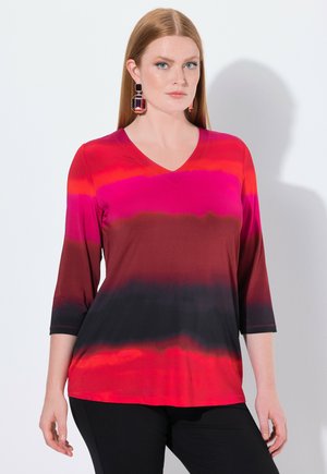 Rotes und pinkes Farbverlauf V-Ausschnitt-Oberteil mit drei Viertelärmeln, glatter Textur und schwarzen Akzenten am Saum. Getragen mit schwarzen Hosen.