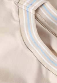 Beige kangas, jossa on sileä pinta ja sinivalkoiset raidat kauluksessa. Yksinkertainen muotoilu, lähikuva.