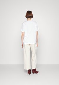 White cotton t-shirt with short sleeves, paired with light beige wide-leg pants and burgundy ankle boots, viewed from the back.
