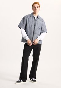 Short-sleeve striped shirt in blue and white, zip front, worn over a white long-sleeve shirt. Black loose-fitting pants and black sneakers.