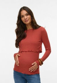 Ribbade, långärmade mammatröja i rostfärg med en vågig nederkant, stylad för en figurnära look, tillsammans med blå jeans och träarmband.