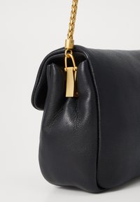 Borsa a spalla in pelle nera con un design morbido, tracolla in catena dorata e dettaglio con lucchetto. Superficie testurizzata con cuciture visibili.