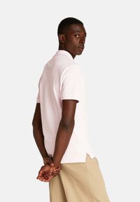 Polo de color rosa claro con mangas cortas, cuello, aberturas laterales y una textura de algodón suave, usado con pantalones cortos caqui.