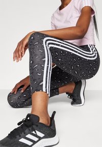 Black and gray leopard print leggings with white stripes on the sides, paired with a light pink cropped t-shirt and black athletic shoes.
