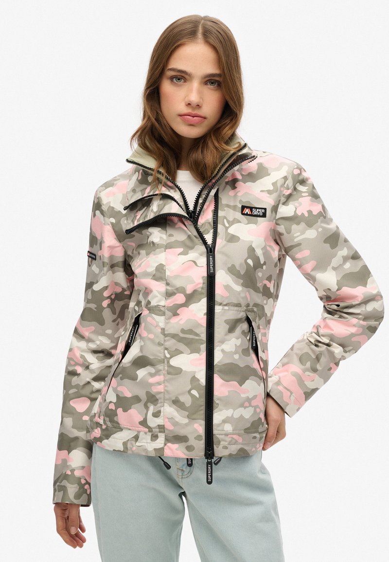 Camouflagejakke i grå, pink og creme farver; har en høj krave, lynlåslommer og justerbart snoretræk i kanten.