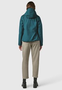 Giubbotto impermeabile turchese con cappuccio, caratterizzato da un design semplice e un vita regolabile con coulisse. Abbinare a pantaloni beige e stivali neri alla caviglia.