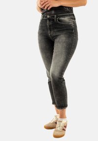 Jeans de tiro alto en gris oscuro, con un acabado ligeramente desgastado. Longitud recortada con dobladillo deshilachado. Combinados con zapatillas beige que cuentan con acentos burdeos.