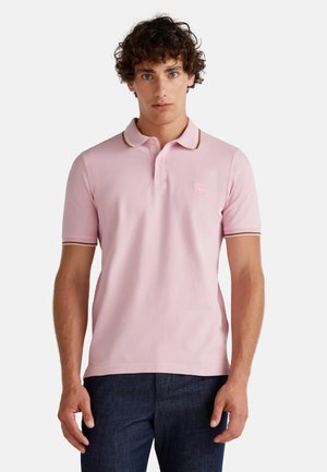 Polo shirt in pastel pink, featuring a classic collar, two-button placket, and contrasting dark stripes on the collar and sleeve edges.