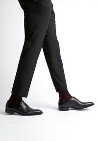 Black leather dress shoes with a polished finish, pointed toe, and subtle stitching details, worn with black trousers and maroon socks.