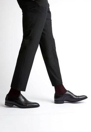 Black leather dress shoes with a polished finish, pointed toe, and subtle stitching details, worn with black trousers and maroon socks.