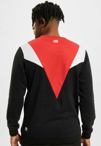 Felpa nera con un audace design triangolare rosso e bianco sul retro, polsini a coste e un piccolo etichetta logo sull'orlo.