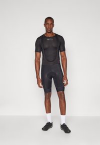 Melnas velosipēda bikses ar sēžamvietu un īsu piedurkņu topu ar acs tekstūru. Iezīmēts ar iešūtu polsteri, elegantu dizainu un logo detaļu. Valkā ar melniem velosipēda apaviem.