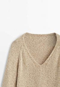 Beige knitted sweater with a V-neckline, featuring a textured pattern and loose fit. The material appears soft and lightweight.