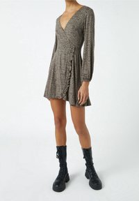 Beige šaty wrap s černými puntíky, s dlouhými nabíranými rukávy, výstřihem do V, volánkovým lemem a rozšířenou sukní. Spárované s černými bojovými botami.