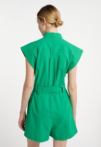 Salopetă verde cu mâneci scurte, cu talie ajustată și curea. Include un guler și un design cu pliuri pe spate. Textură netedă din bumbac.