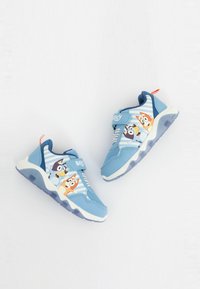 Baskets bleues pour enfants avec des personnages de chiens de dessin animé, bandes velcro, semelles blanches et languettes orange sur fond blanc.