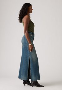 Blå denim maxi-skjørt med sidespalter, høy midje og subtil fading. Kombinert med en olivengrønn tank top og svarte spisse ankelstøvler.