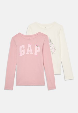 Two long-sleeve shirts: one pink with "GAP" logo in white and decorative accents, and one ivory with a graphic print. Cotton fabric, casual style.