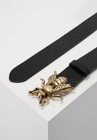 Black leather belt featuring a detailed, metallic gold insect-shaped buckle. The belt has evenly spaced holes for adjustments.