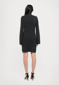 Sötétszürke, hosszú ujjú ruha, testhezálló sziluettel, térd alatt végződő szegéllyel és textúrált anyaggal. Fekete magassarkú szandálokkal viselve.