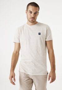 Camiseta de rayas beige de algodón, con cuello redondo, mangas cortas y un pequeño parche azul marino en el área del pecho izquierdo.