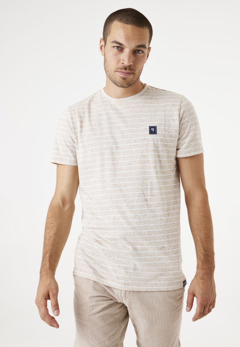 Camiseta de rayas beige de algodón, con cuello redondo, mangas cortas y un pequeño parche azul marino en el área del pecho izquierdo.