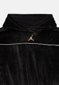 Czarna bluza z weluru z złotym logo Jumpman umieszczonym na środku poniżej kaptura oraz białym wykończeniem wzdłuż klatki piersiowej.