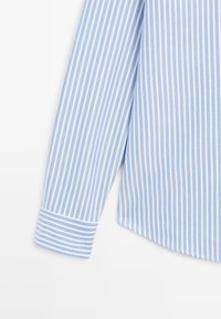 Manica di camicia a righe bianche e azzurre, con un polsino a righe contrastanti. La trama del tessuto sembra liscia, con un design classico e su misura.