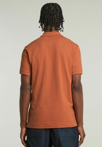 Polo a maniche corte di colore ruggine. Realizzato in cotone, dotato di colletto classico e polsini a coste. Tessuto morbido, design essenziale.