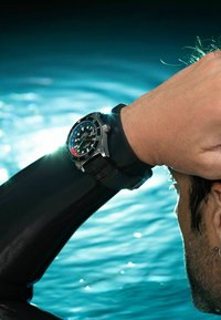 Duikhorloge met een zwarte rubberen band en een roestvrijstalen kast; heeft een zwart wijzerplaat met blauwe en rode accenten, grote luminescente markeringen.