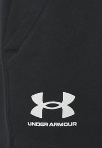 Pantalones cortos de algodón negros con un bolsillo lateral y un logo de Under Armour en blanco. Textura suave con un diseño limpio y moderno.