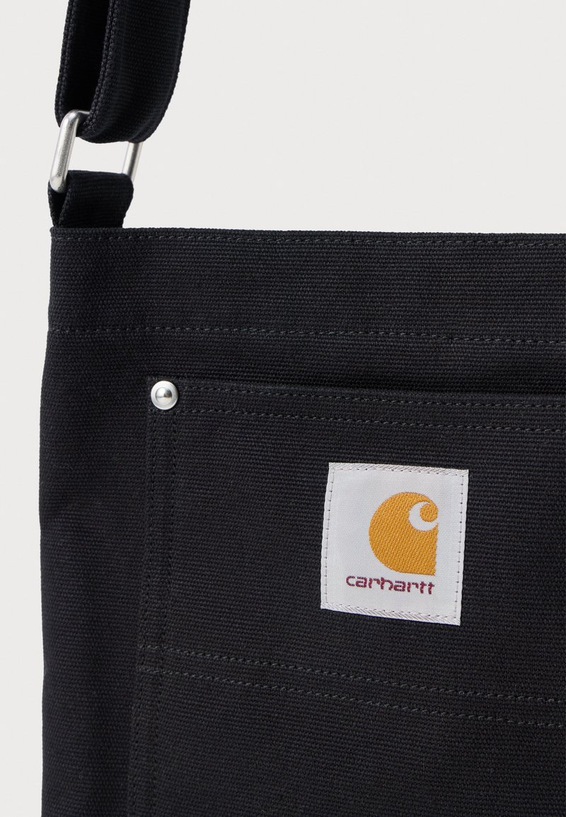 Black canvas shoulder bag with front pocket and Carhartt logo patch in yellow and white stitching visible.
