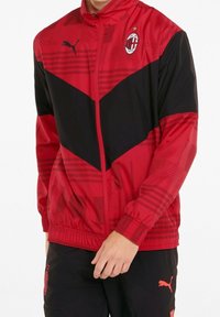 Leichte Jacke in Rot und Schwarz mit Reißverschluss, ausgestattet mit einem Chevron-Design, strukturierten Mustern und Logo-Akzenten von Puma und AC Milan.
