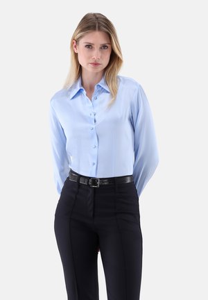 Camicia azzurro chiaro con collo e maniche lunghe, abbinata a pantaloni aderenti neri e una cintura nera texturizzata.