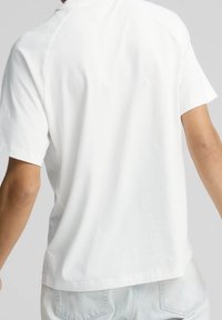 Camiseta de algodón blanca con un corte relajado, mangas cortas y cuello redondo. Textura suave y diseño minimalista, con una vista trasera sencilla.