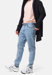 Jean en denim bleu clair avec une coupe décontractée, associé à un T-shirt rose et un long cardigan noir. Des baskets blanches complètent la tenue.