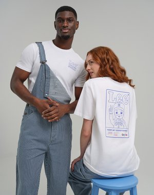 Uomo in salopette a righe e t-shirt bianca Lee Crayola, donna con capelli rossi seduta su uno sgabello blu che indossa una t-shirt bianca Lee con grafiche sul retro.