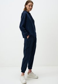 Sweat-shirt à capuche bleu marine avec coupe ample, poignets élastiques, associé à un pantalon bleu marine fuselé avec poches latérales et chevilles élastiques.