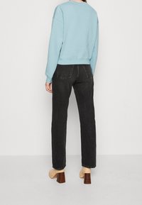 Ljusblå sweatshirt med en kortad design, kombinerad med högmidjade svarta jeans. Skorna är beige med en träblockklack.