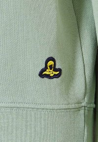 Lichtgroene sweatshirtstof met ribbeltextuur. Heeft een klein geborduurd logo in geel en marineblauw op het lagere gedeelte.