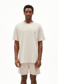 Lichtbeige oversized t-shirt met geribde ronde hals en korte mouwen, met een klein geborduurd logo op de borst. Gekleed met bijpassende beige shorts.