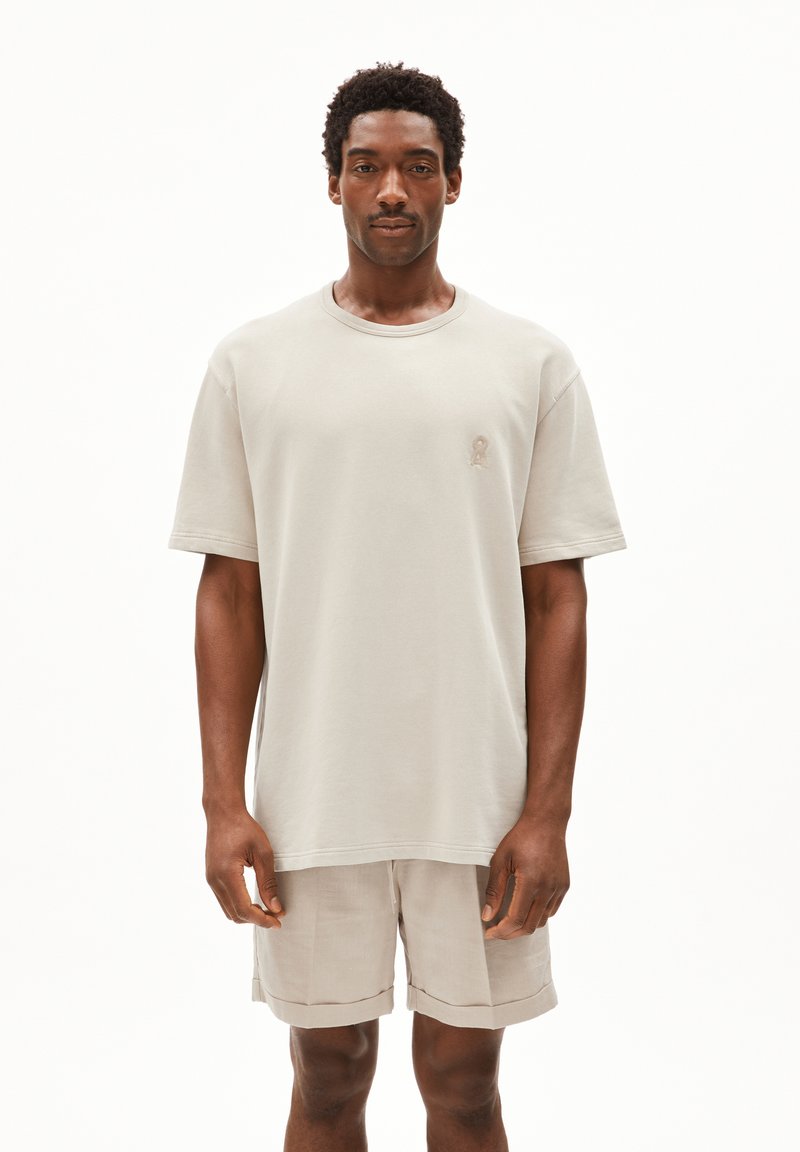 Lichtbeige oversized t-shirt met geribde ronde hals en korte mouwen, met een klein geborduurd logo op de borst. Gekleed met bijpassende beige shorts.