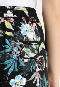 Pantalon noir à motif floral coloré avec des fleurs bleues et roses. Conçu avec une taille élastique et une poche latérale.