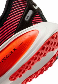 Sneaker nera con tomaia in tessuto a righe rosse e rosa, suola intermedia bianca e dettaglio arancione sul tallone. Il battistrada presenta motivi in gomma rossa in rilievo.
