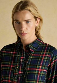 Navy plaid shirt featuring red and green lines, a button-down design, and a ruffled placket. Soft fabric with a collared neckline.